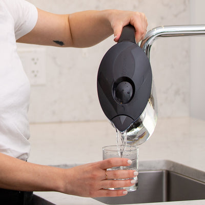 A woman pouring clean water from the Santevia MINA Alkaline Pitcher in black into glass#color_black