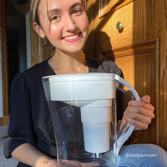 @localplanteater A woman sitting crossed legged smiling and holding her white Santevia MINA Alkaline Pitcher